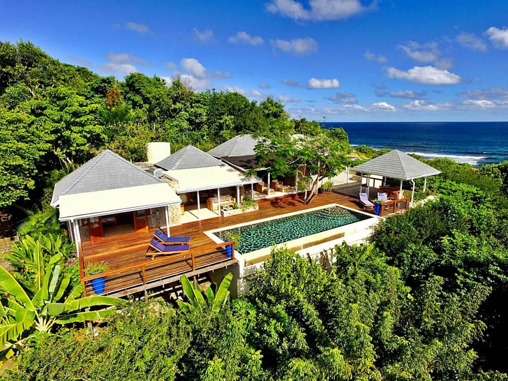 Aerial view of Crescent Beach Villa on Crescent Beach, Bequia — showing the villa, infinity pool, tropical gardens, and the Atlantic Ocean in the background. Featured on the Real Grenadines Villa Rentals website.
